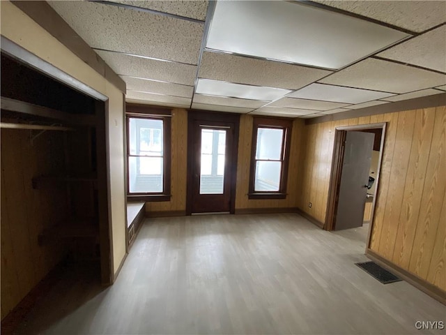 unfurnished room with a drop ceiling, light wood-style flooring, wood walls, visible vents, and baseboards