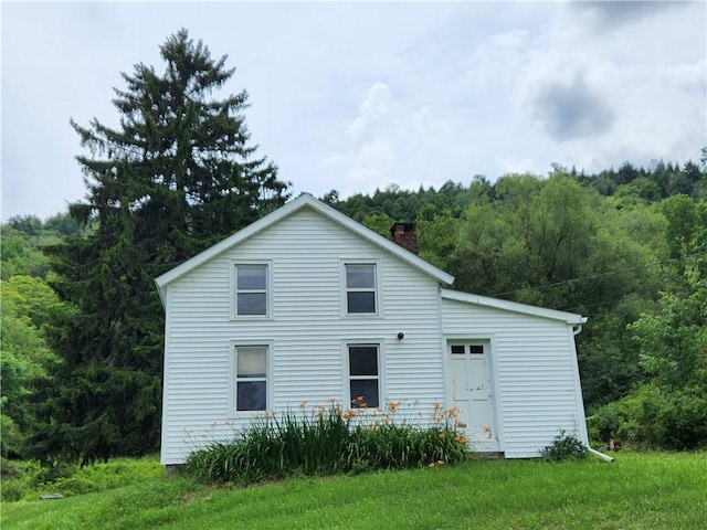 view of front facade featuring a front yard, a forest view, and a chimney