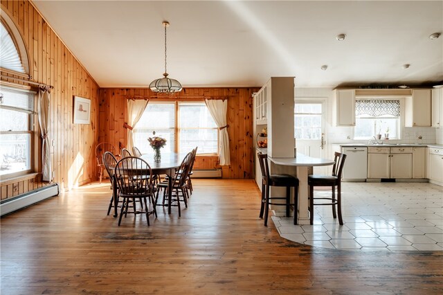 dining room with light hardwood / wood-style floors, a baseboard radiator, plenty of natural light, and wood walls