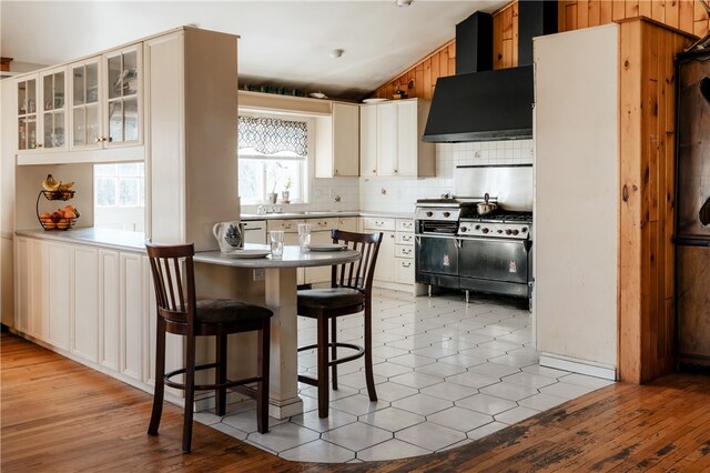 kitchen featuring tasteful backsplash, light hardwood / wood-style flooring, wall chimney range hood, and high end range oven