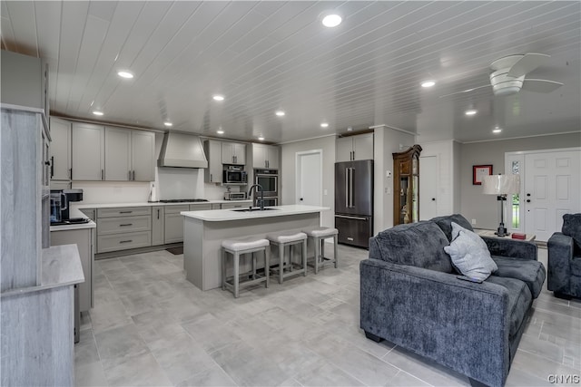 kitchen with a kitchen island with sink, ceiling fan, sink, custom range hood, and stainless steel appliances