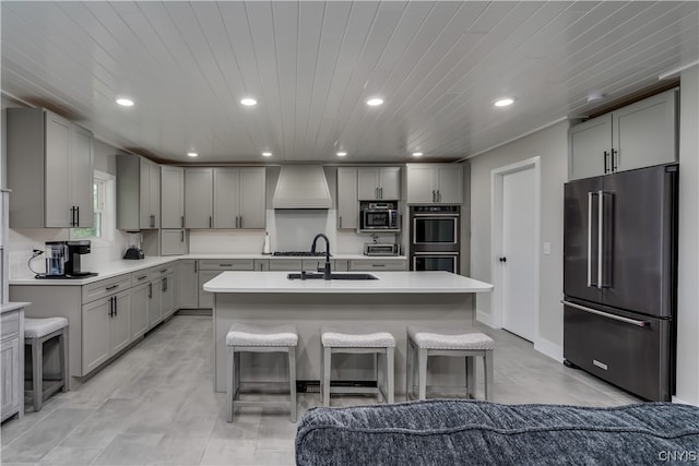 kitchen with sink, appliances with stainless steel finishes, a center island with sink, light tile flooring, and custom exhaust hood