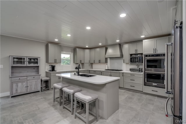 kitchen with stainless steel appliances, a center island with sink, gray cabinets, custom range hood, and sink