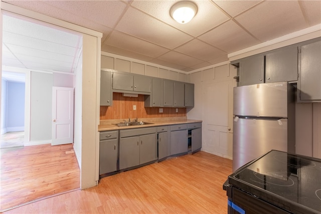 kitchen with a paneled ceiling, light hardwood / wood-style flooring, sink, stainless steel refrigerator, and black range