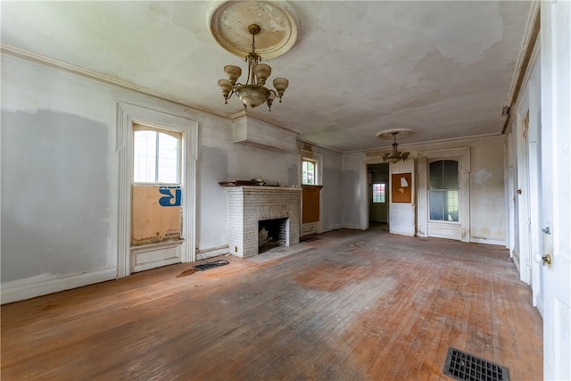 unfurnished living room featuring an inviting chandelier, ornamental molding, dark wood-type flooring, and a brick fireplace