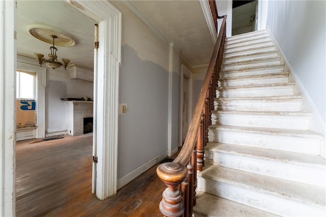stairs with crown molding, dark hardwood / wood-style flooring, a fireplace, and a chandelier