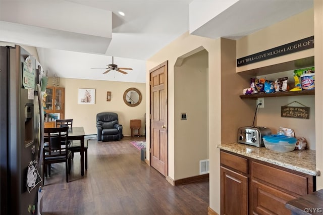 interior space with dark wood-type flooring, ceiling fan, stainless steel fridge, and light stone counters