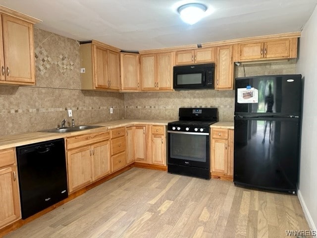 kitchen with backsplash, black appliances, sink, and light hardwood / wood-style flooring