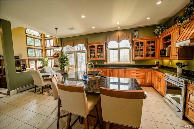 kitchen featuring sink, decorative light fixtures, stainless steel stove, light tile patterned flooring, and an island with sink