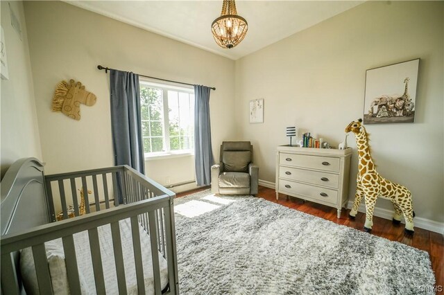 bedroom with dark wood-type flooring, an inviting chandelier, and a crib