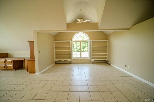 empty room with built in desk, ceiling fan, light tile patterned flooring, high vaulted ceiling, and a baseboard radiator