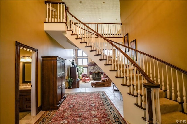 stairs with sink, a high ceiling, tile patterned floors, and a stone fireplace