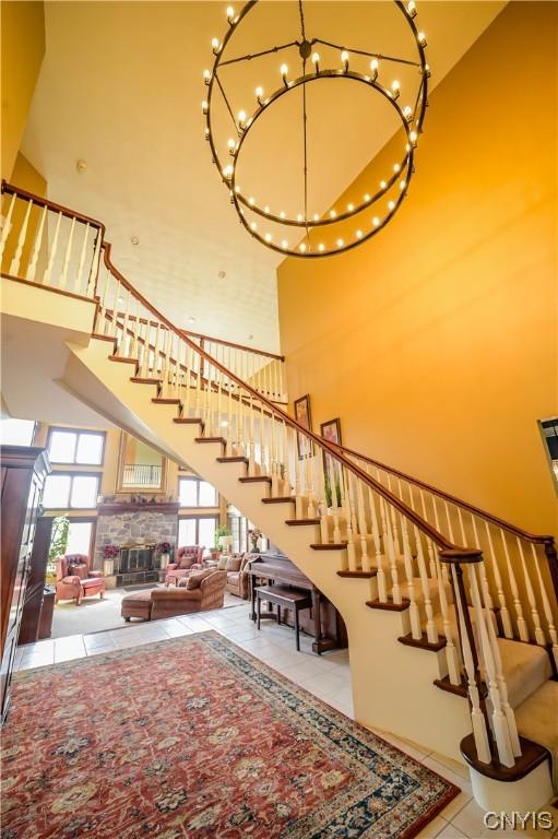 staircase with a towering ceiling, tile patterned floors, a wealth of natural light, and a stone fireplace