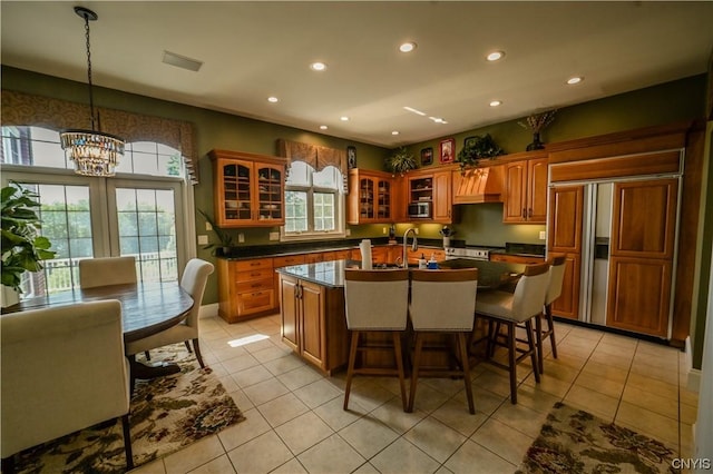 kitchen with a kitchen bar, light tile patterned floors, an island with sink, hanging light fixtures, and a chandelier