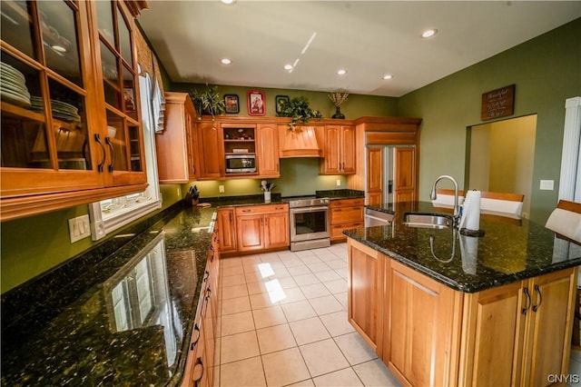 kitchen featuring appliances with stainless steel finishes, an island with sink, light tile patterned floors, dark stone counters, and sink