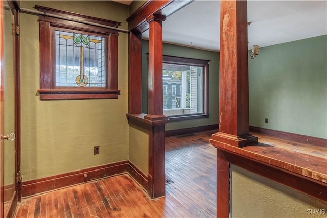 interior space featuring baseboards, decorative columns, and hardwood / wood-style floors