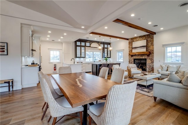 dining room with a fireplace, beamed ceiling, a healthy amount of sunlight, and light wood-type flooring