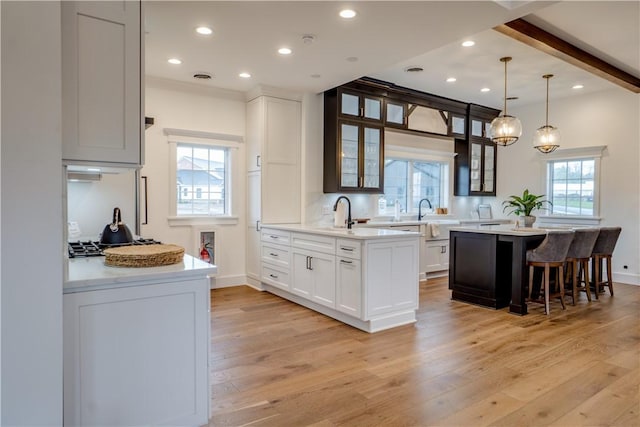 kitchen with pendant lighting, a center island, white cabinets, light hardwood / wood-style flooring, and beamed ceiling