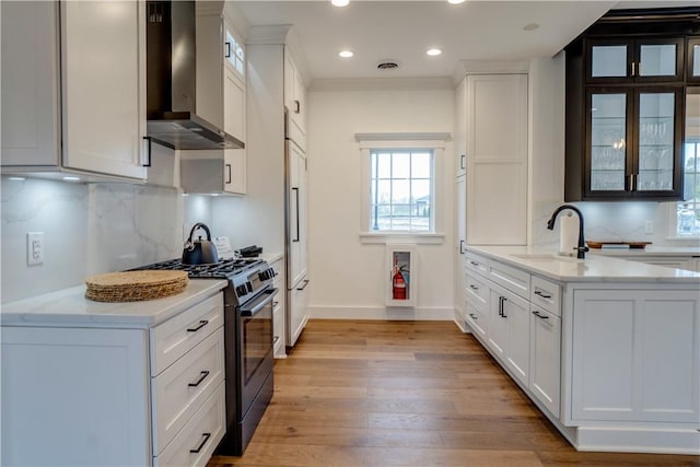 kitchen with white cabinets, wall chimney exhaust hood, stainless steel gas range oven, and light wood-type flooring