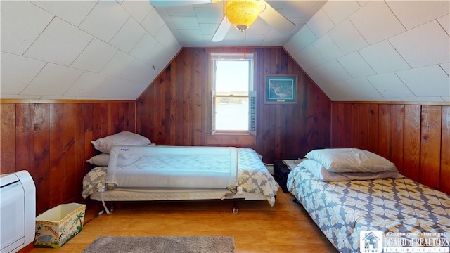 bedroom with light hardwood / wood-style flooring, ceiling fan, wooden walls, and vaulted ceiling