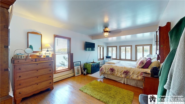 bedroom with ceiling fan, baseboard heating, light wood-type flooring, and multiple windows