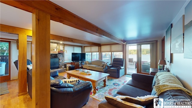 living room featuring light hardwood / wood-style flooring, beam ceiling, and a stone fireplace