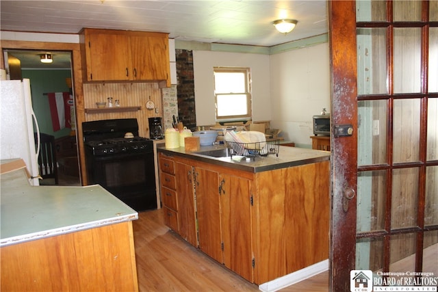 kitchen with black range with gas stovetop, white fridge, light wood-type flooring, and sink