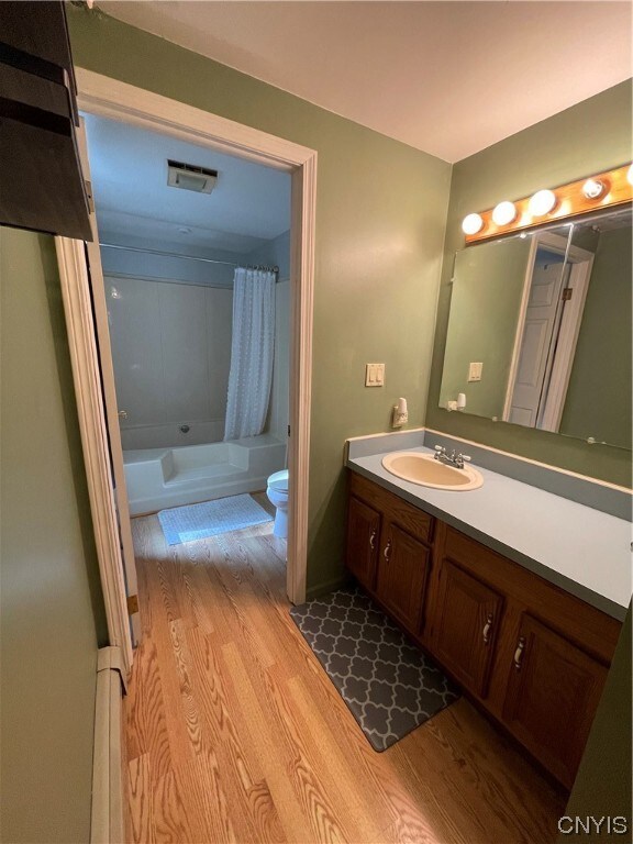 full bathroom with shower / tub combo, hardwood / wood-style floors, large vanity, and toilet