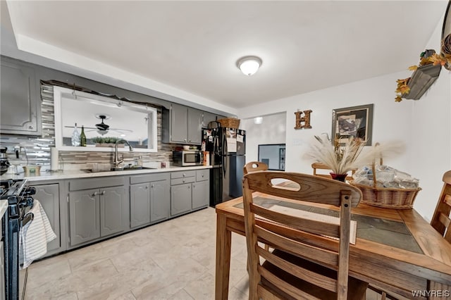 kitchen with sink, light tile floors, gray cabinetry, backsplash, and stainless steel appliances