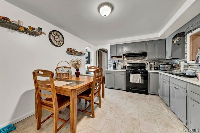 kitchen with tasteful backsplash, gray cabinetry, ventilation hood, black gas range oven, and light tile flooring