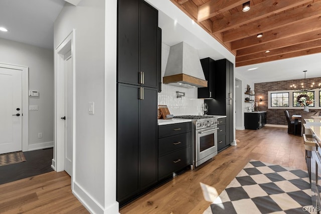 kitchen with tasteful backsplash, light wood-type flooring, high end range, premium range hood, and beam ceiling