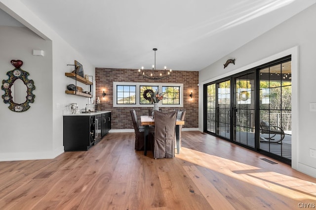 dining room featuring dark hardwood / wood-style flooring, a notable chandelier, brick wall, and a wealth of natural light