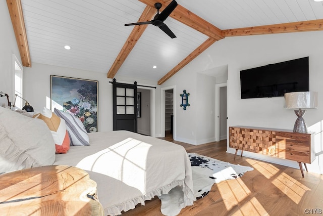 bedroom featuring a barn door, dark hardwood / wood-style floors, ceiling fan, lofted ceiling with beams, and a walk in closet