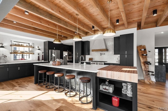 kitchen featuring backsplash, a center island with sink, light hardwood / wood-style floors, and premium range hood