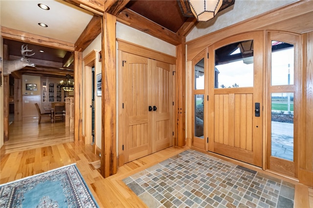 entryway with beam ceiling, a chandelier, and light hardwood / wood-style flooring