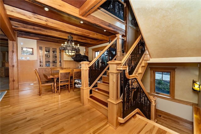 stairs featuring built in features, hardwood / wood-style flooring, an inviting chandelier, and beam ceiling