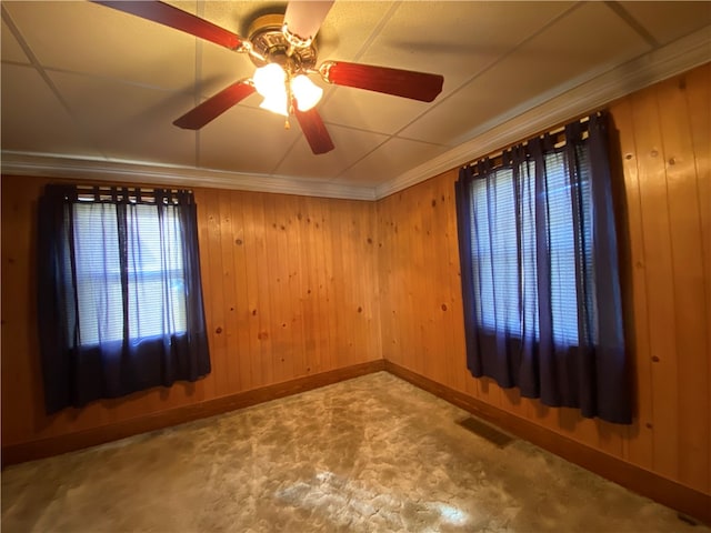 spare room featuring carpet flooring, ornamental molding, wooden walls, and ceiling fan