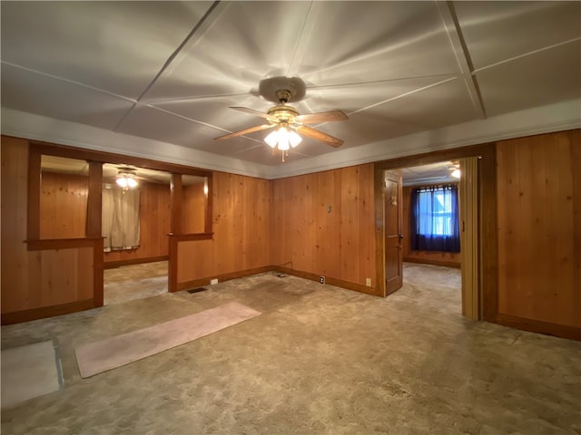 basement featuring wood walls, light carpet, and ceiling fan