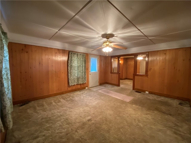 basement featuring wooden walls, ceiling fan, and light colored carpet