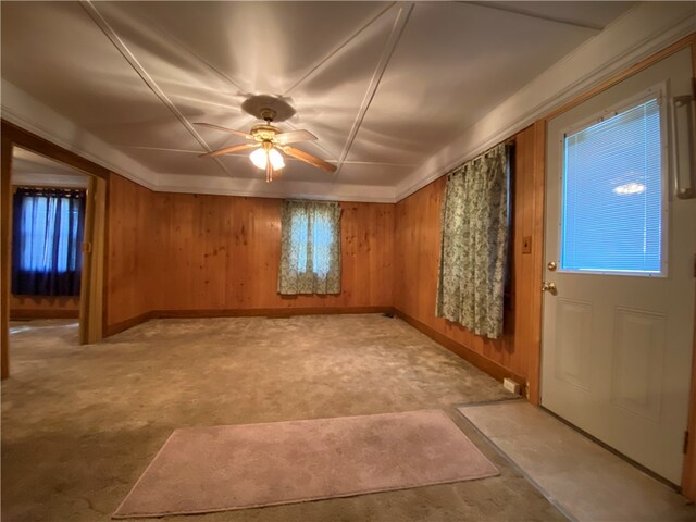 carpeted spare room featuring wood walls and ceiling fan