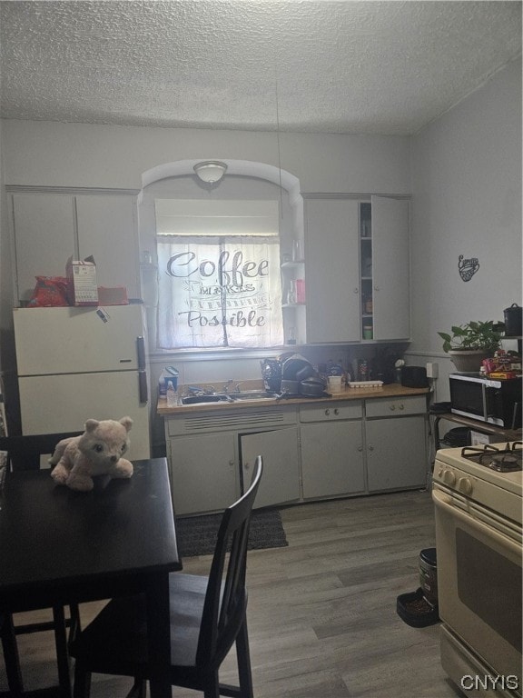 kitchen with white appliances, hardwood / wood-style floors, white cabinets, sink, and a textured ceiling