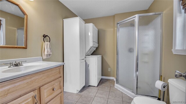 bathroom featuring vanity, tile patterned floors, stacked washer and dryer, toilet, and an enclosed shower