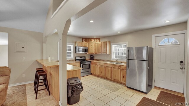 kitchen with light brown cabinets, a kitchen breakfast bar, sink, light tile patterned floors, and appliances with stainless steel finishes