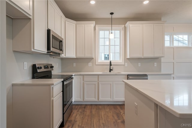 kitchen with stainless steel appliances, decorative light fixtures, dark wood-type flooring, white cabinets, and sink