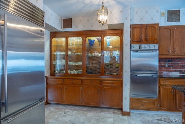 kitchen featuring dark stone counters, multiple ovens, stainless steel built in fridge, and hanging light fixtures