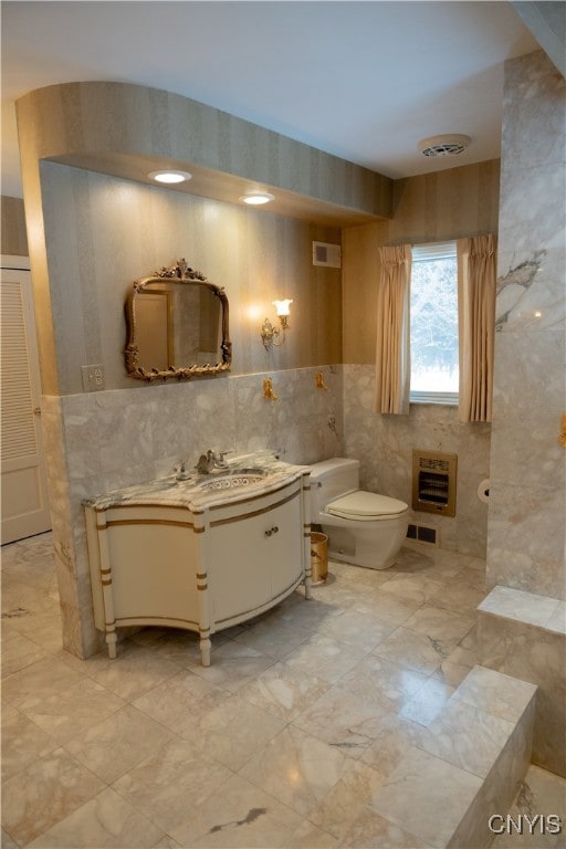 bathroom with tile walls, heating unit, vanity, and toilet