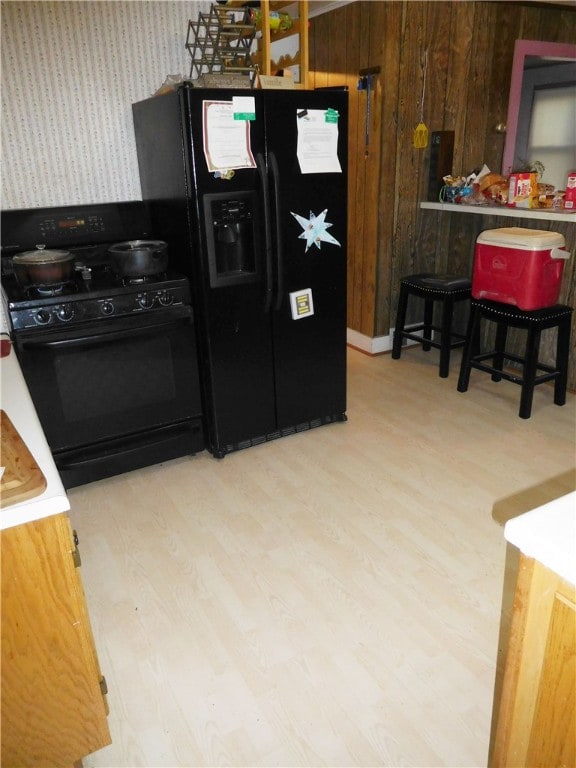 kitchen featuring black appliances, wood walls, light hardwood / wood-style flooring, and a breakfast bar