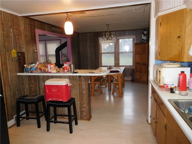 kitchen with wooden walls, hanging light fixtures, a kitchen breakfast bar, and light hardwood / wood-style flooring