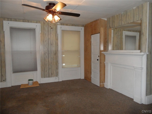 unfurnished living room with wooden walls, dark carpet, and ceiling fan