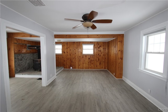 spare room featuring a wood stove, ceiling fan, a wealth of natural light, and light wood-type flooring